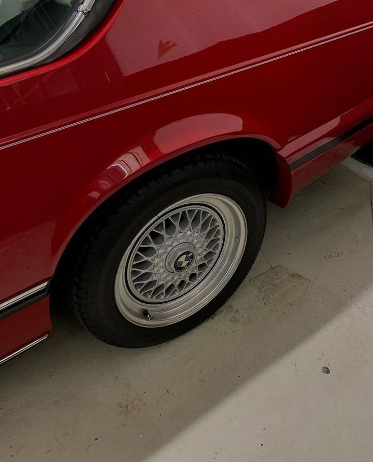 a red car parked in a garage next to a white dog laying on the ground