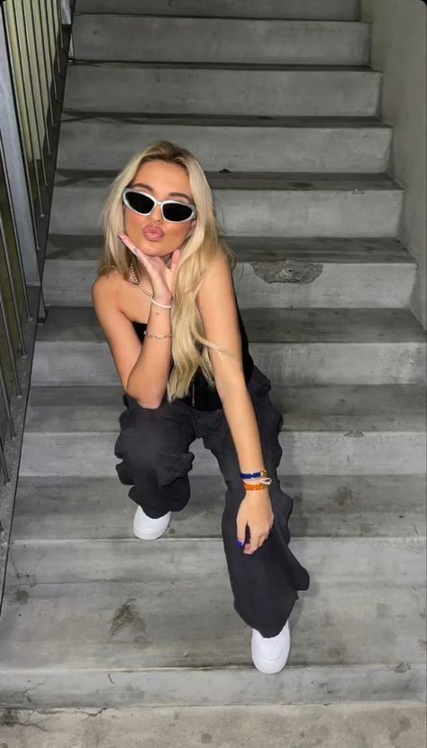 a woman sitting on some stairs with her hand under her chin and wearing sunglasses over her eyes