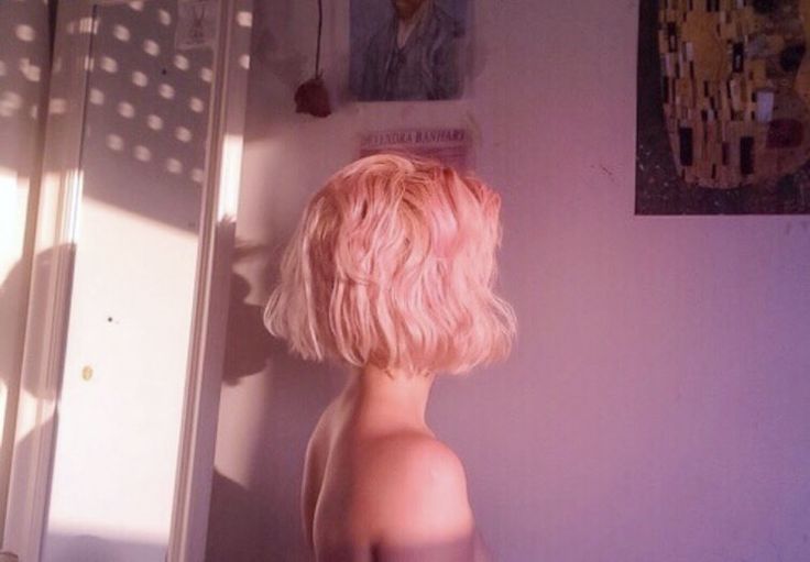 a naked woman with pink hair standing in front of a bathroom mirror and looking at her reflection