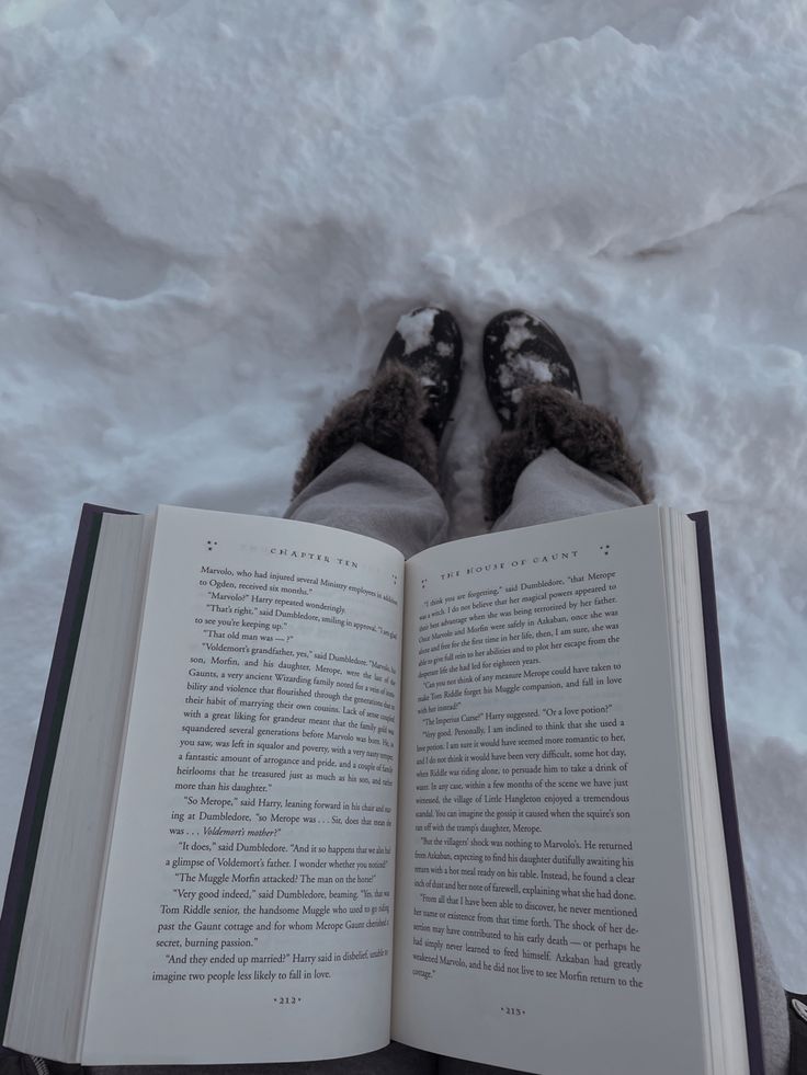 someone is reading a book in the snow with their feet propped up on top of it