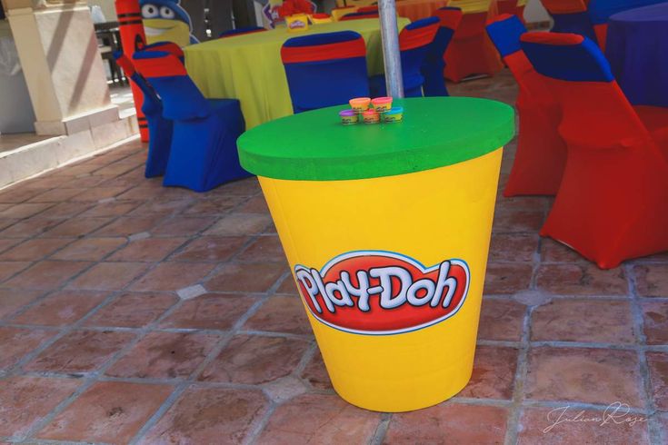 a large yellow cup sitting on top of a floor next to colorful tables and chairs