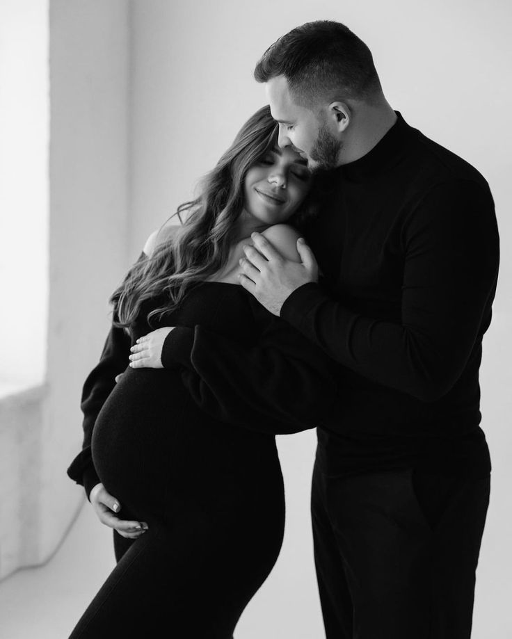 a pregnant couple cuddles in black and white for their newborn photo session at the studio