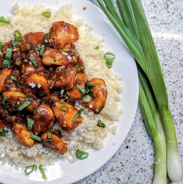 a white plate topped with chicken and rice next to green onions on top of a table