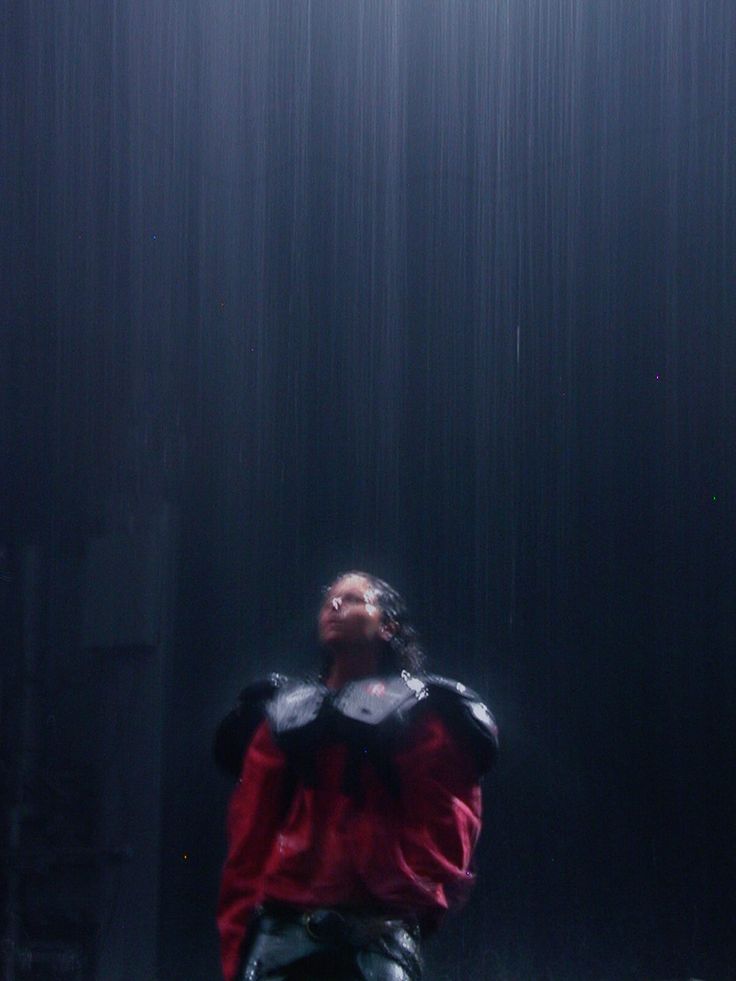 a man is standing in the rain with his arms outstretched and head tilted to the side