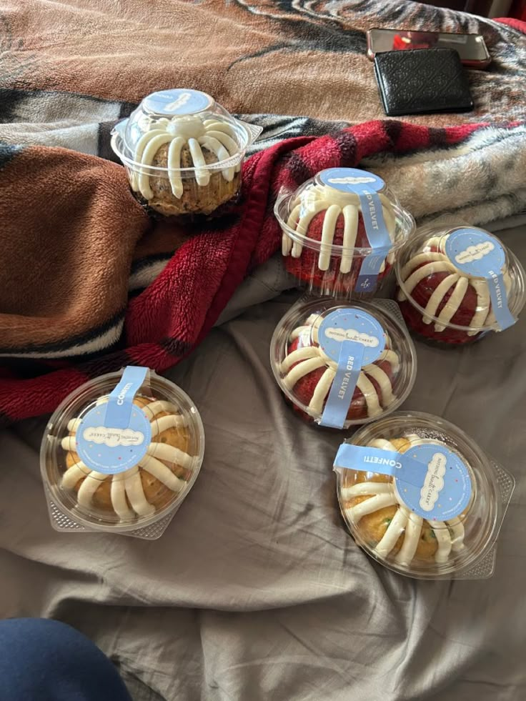 four plastic containers filled with food sitting on top of a bed next to a blanket