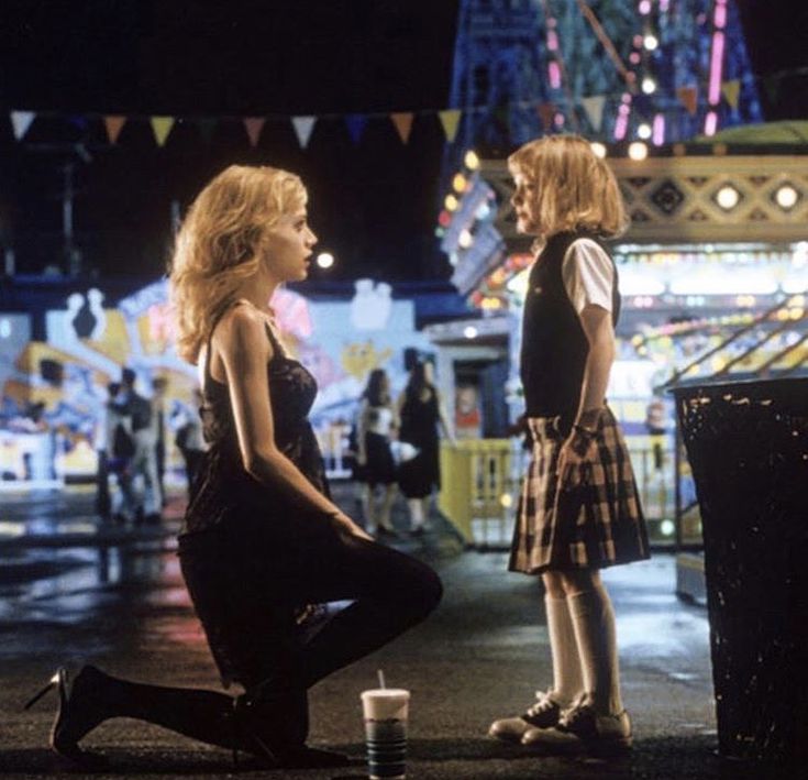 two young women standing next to each other in front of a carnival ride at night