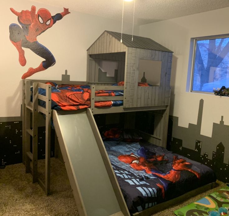 a child's bedroom with bunk beds and a slide in the middle, spiderman mural on the wall