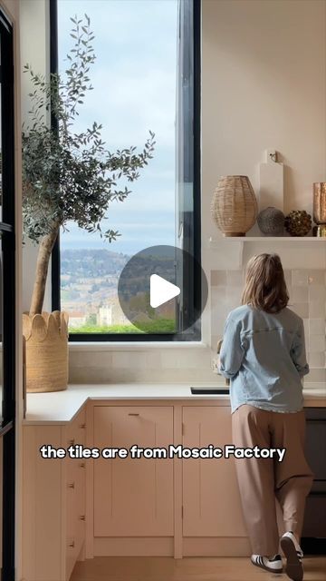 a woman standing in front of a kitchen window looking out at the city below her