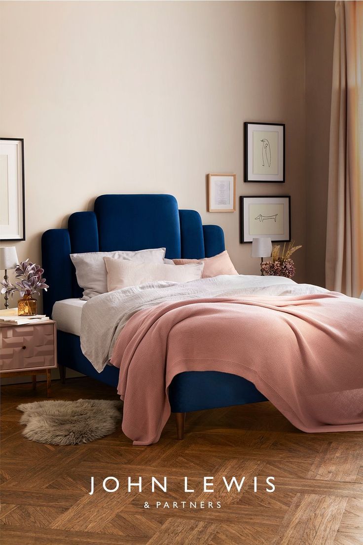 a bed with pink sheets and pillows in a bedroom next to a wooden flooring