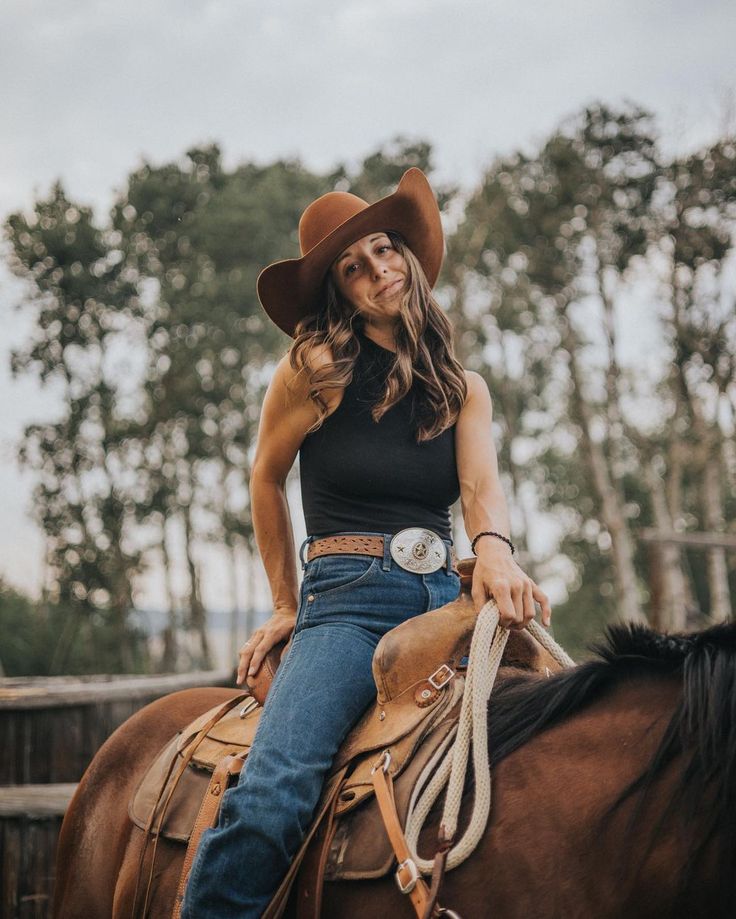 a woman sitting on top of a brown horse wearing a cowboy hat and black shirt