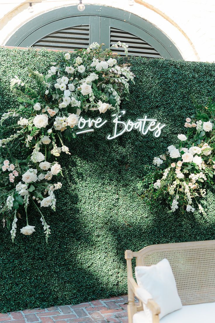 an outdoor seating area with white flowers and greenery on the wall that says one boat