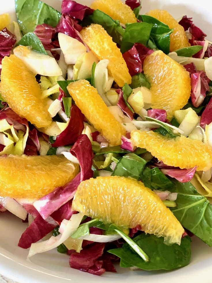 a salad with oranges, lettuce and other vegetables in a white bowl