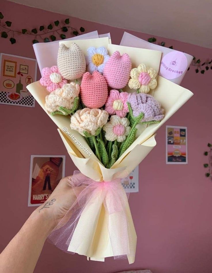 a hand holding a bouquet of crocheted flowers in pink, white and yellow colors