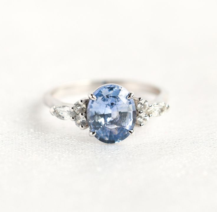 an oval blue and white sapphire ring with three diamonds on the sides, set in 18k white gold