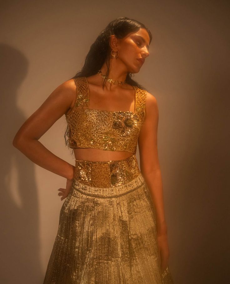 Step into refined elegance with the goldusion ensemble, where traditional craftsmanship meets modern innovation. The metallic lehenga, crafted from hand-crushed gold fabric, exudes opulence, while the detachable corset belt and blouse are fully embellished for added glamour. Architectural embroidery, inspired by mughal lattice motifs, adds a striking, textured dimension. A masterful fusion of texture, form, and cultural heritage, this ensemble redefines contemporary sophistication. Gold Brocade Pre-draped Saree With Zari Work, Festive Gold Embellished Pre-draped Saree, Gold Pre-draped Saree For Diwali Reception, Gold Pre-draped Saree For Reception And Festive Occasions, Fitted Gold Pre-draped Saree For Festive Occasions, Festive Gold Pre-draped Saree With Sequins, Glamorous Gold Party Sets, Gold Pre-draped Saree With Cutdana For Party, Gold Pre-draped Saree For Navratri Party