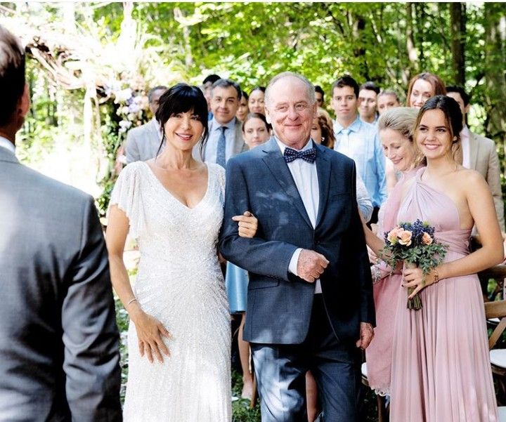 a man and woman are walking down the aisle with other people in the back ground