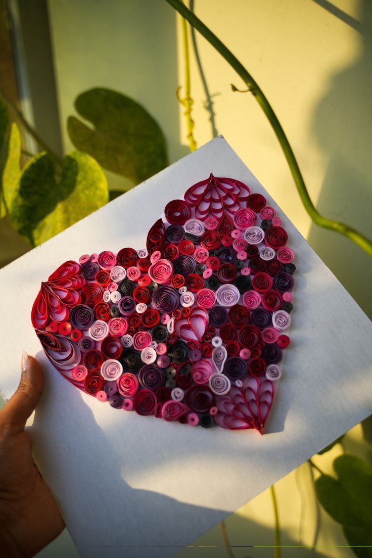 a heart made out of buttons sitting on top of a piece of paper next to a plant