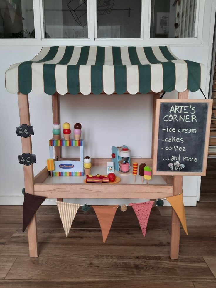 an outdoor ice cream stand is decorated with flags and bunting on the outside, while a chalkboard sign reads artee's corner