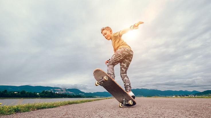 a young man riding a skateboard on top of a gravel covered road next to a lake