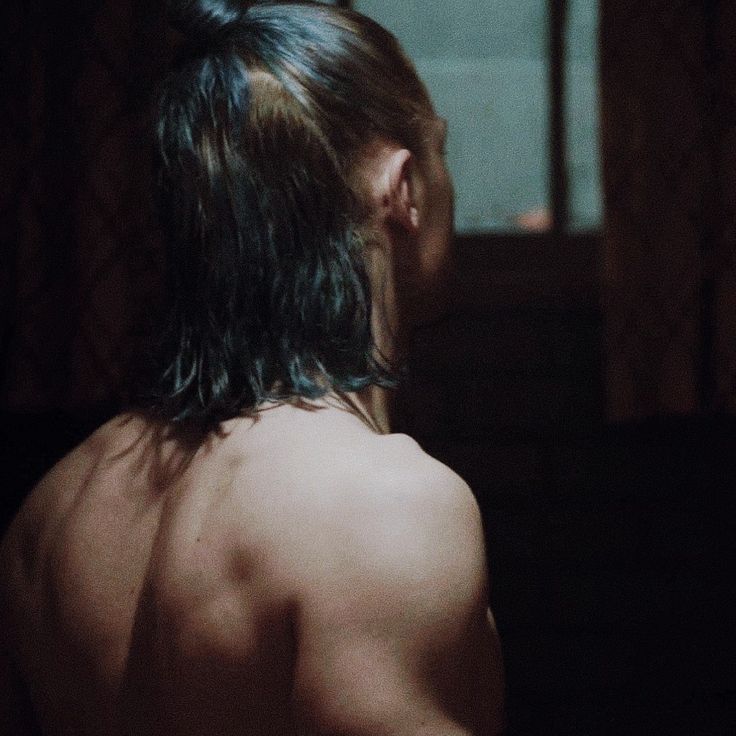 a man with long hair standing in front of a mirror looking at his reflection on the wall