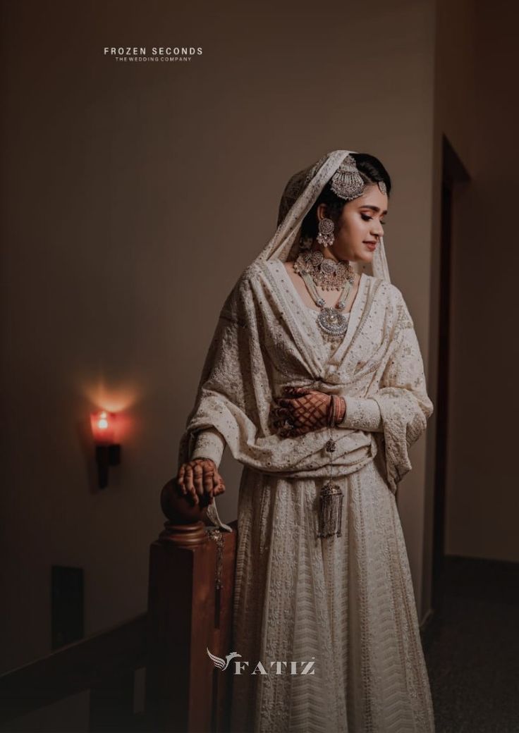 a woman in a white wedding dress holding a suitcase and looking at the camera while standing next to a candle