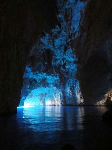 the inside of a cave lit up with blue lights and water in front of it