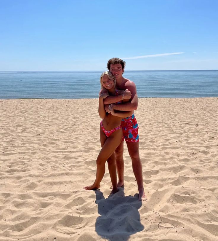 two people hugging each other on a sandy beach with the ocean and sky in the background