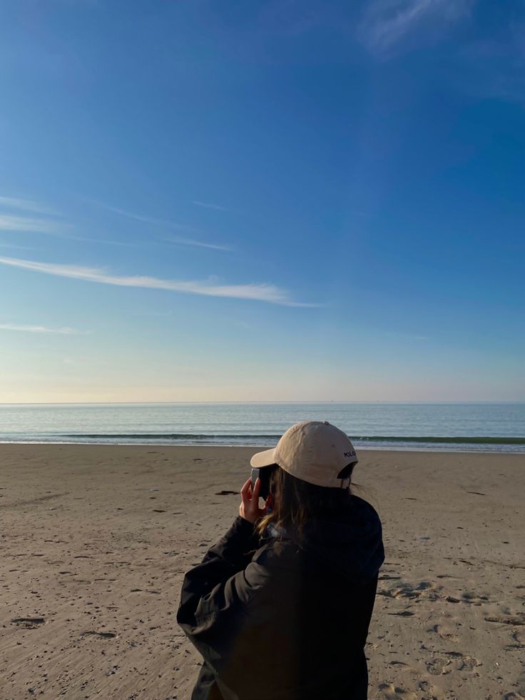 a woman sitting on top of a sandy beach next to the ocean under a blue sky