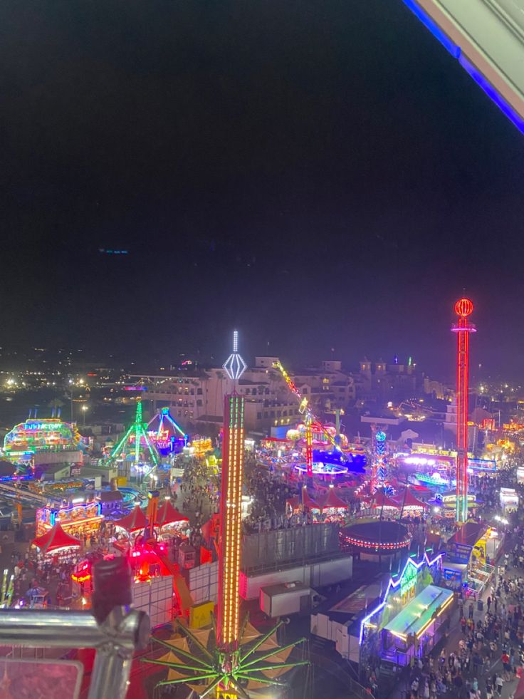 an aerial view of a carnival at night with lights on and rides in the background