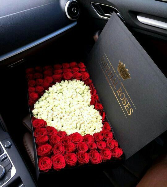 a heart shaped box filled with roses in the back seat of a car, next to a book