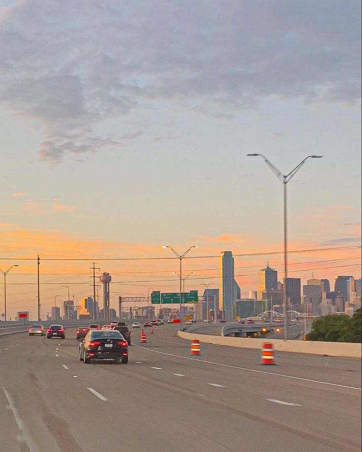 cars are driving down the highway in front of an orange and yellow traffic cone at sunset