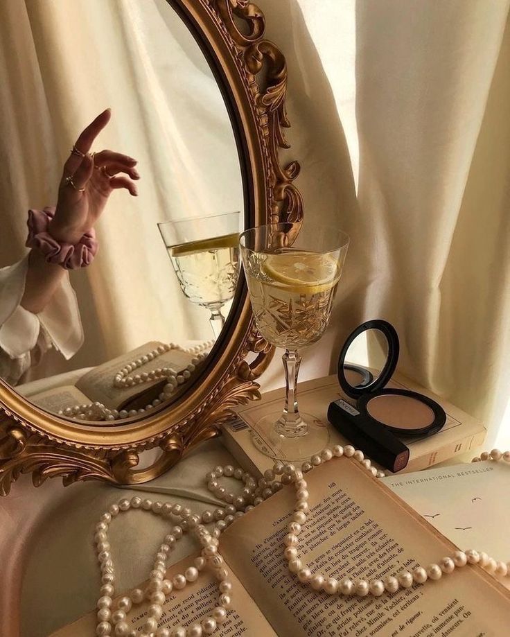 an open book with pearls on it and a glass of wine in front of the mirror