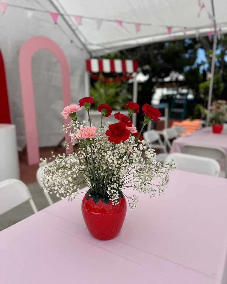 a vase filled with red and white flowers on top of a table next to chairs