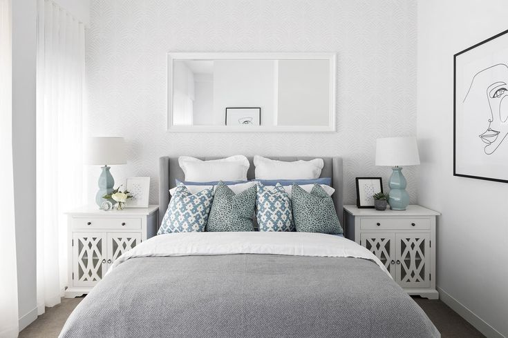 a bedroom with white walls and grey bedding, two nightstands and a framed portrait on the wall