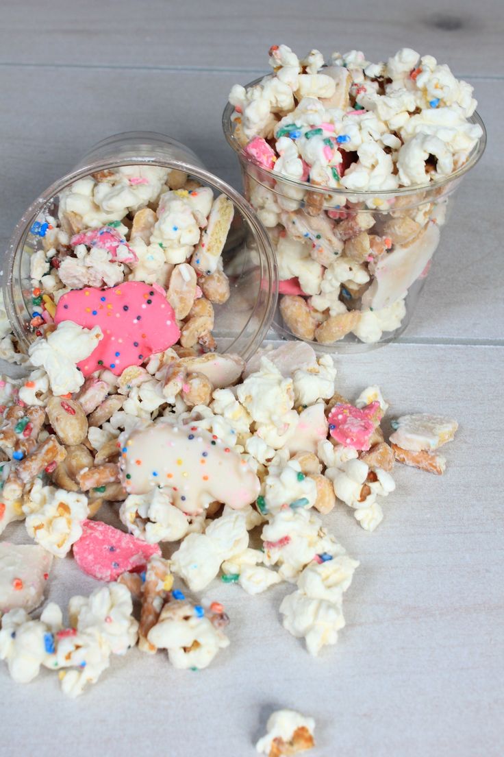 two cups filled with popcorn and sprinkles on top of a wooden table