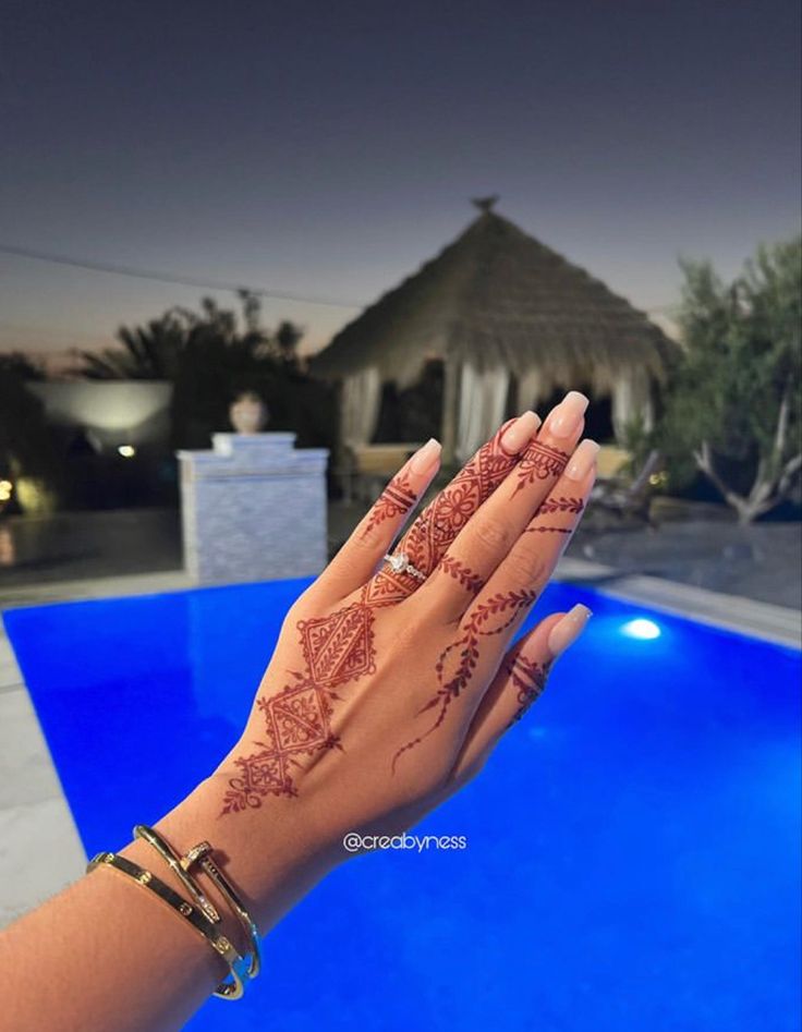 a woman's hand with henna on it next to a swimming pool