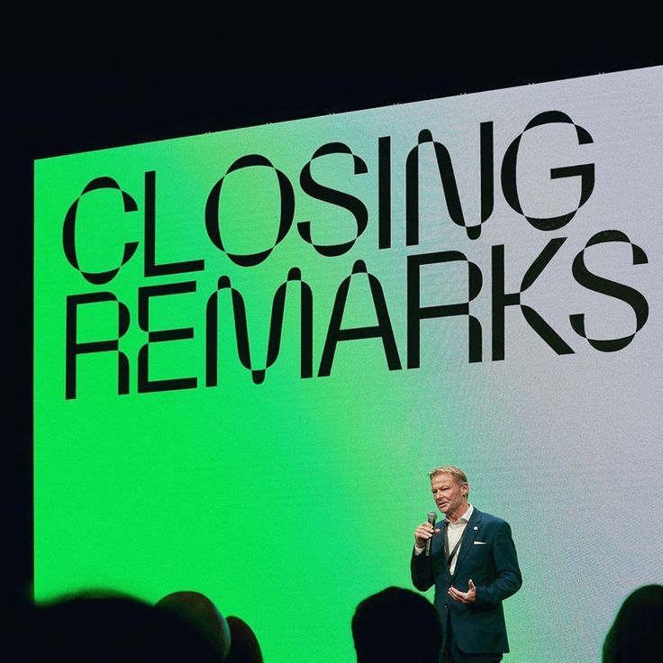 a man standing in front of a green screen giving a speech at a closing rehmarks event