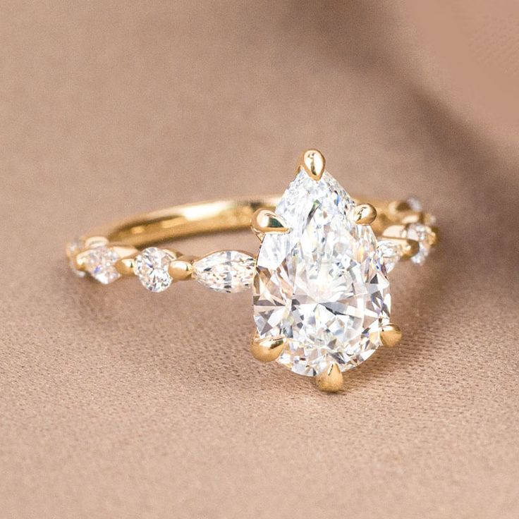 an oval cut diamond ring with pear shaped diamonds on the band and side stones in yellow gold