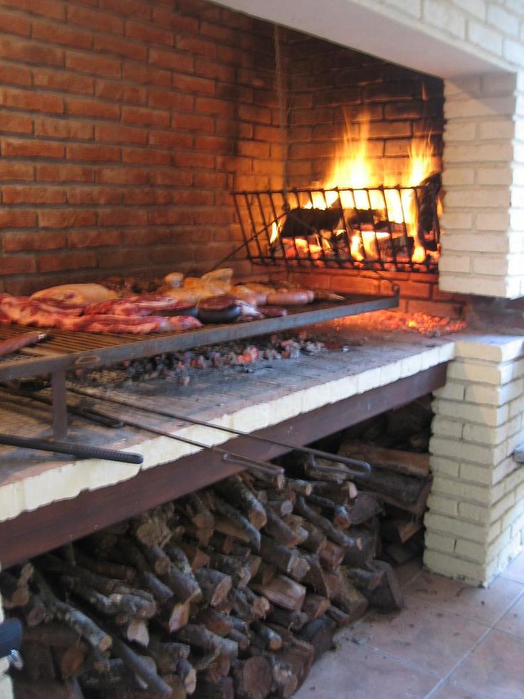 a brick oven filled with lots of meat on top of it's sides next to a pile of firewood