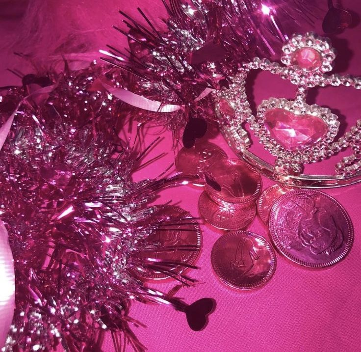 a pink table topped with lots of different types of coins and tiara crowns on top of each other