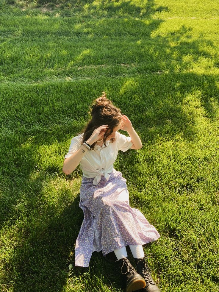 a woman sitting in the grass with her head on her hands and looking at something