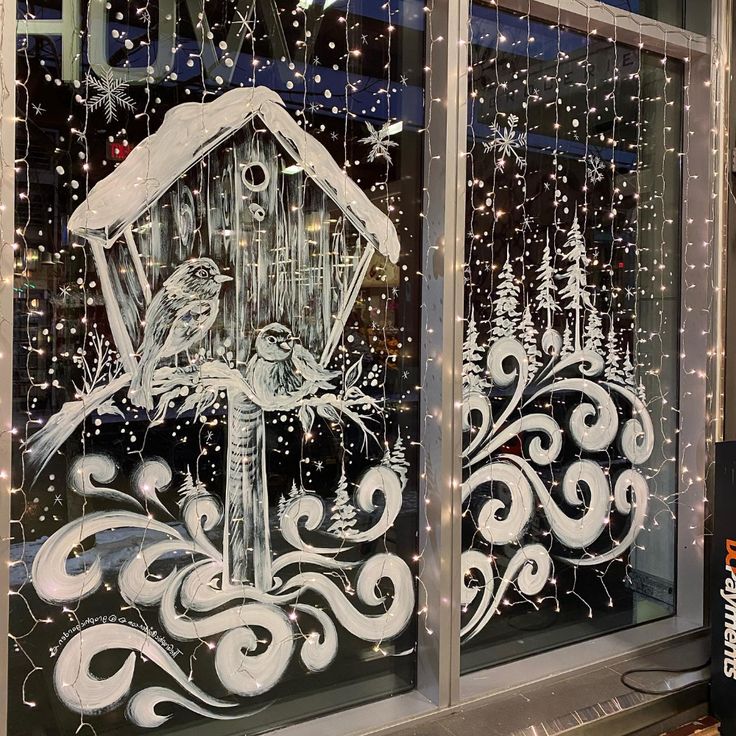 two glass windows decorated with christmas scenes and birds in the snow, one is holding a birdhouse