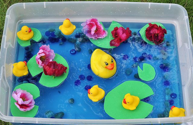 a plastic container filled with water and rubber ducks floating on top of lily pads in a pond