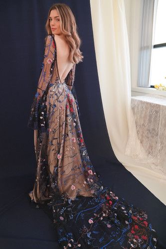 a woman standing in front of a window wearing a long dress with flowers on it