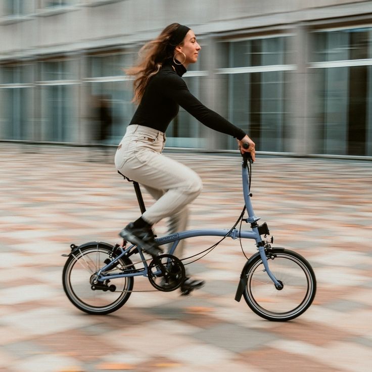 a woman riding a bike with a leash on the handlebars in front of a building