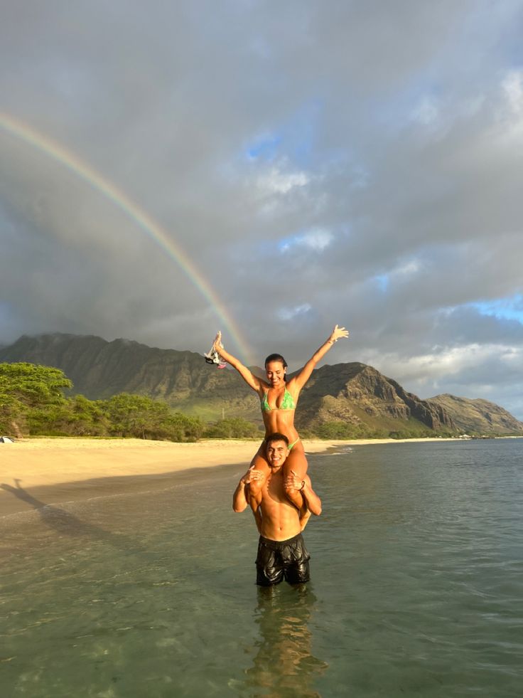 two people standing in the water with a rainbow behind them