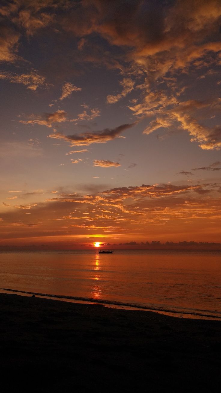 the sun is setting over the ocean with clouds in the sky