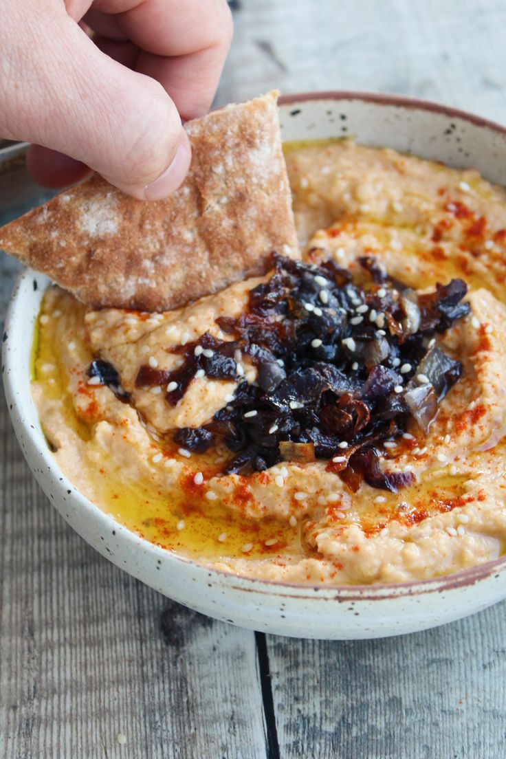 a hand holding a cracker over a bowl of hummus with raisins