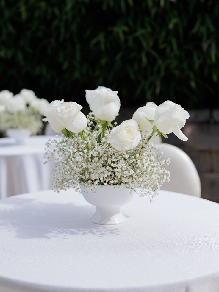 white roses and baby's breath in a vase on a round table with chairs