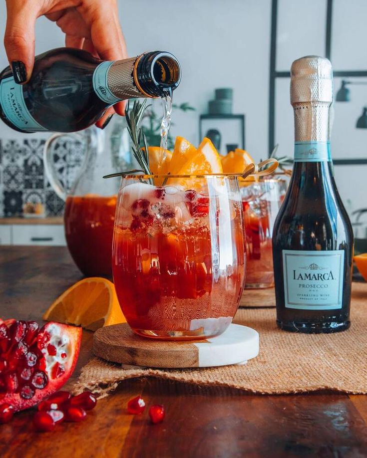 someone pouring wine into a glass with oranges and pomegranate